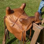 Reconstructed Connolly four-horned saddle (reconstruction Comitatus). Image: MCB Reconstructed Roman saddle displayed on a wooden stand. It has a light tan leather cover, four hors (one at each corner, and straps hanging from each one.