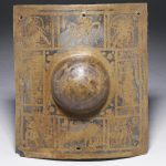 Curved rectangular copper-alloy shield boss from the River Tyne at South Shields with a hemispherical boss, engraved and punctim decoration, and selective tinning. Image: © The Trustees of the British Museum (CC BY-NC-SA 4.0) Front view of a curved rectangular shield boss with a yellowy and silver patine and with a hemispherical boss.