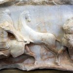 Detail of the Aemilius Paullus monument showing Macedonian cavalry and a Roman legionary. His large, curved, oval shield with a horizontal hand grip is clearly visible. The figure is heavily damaged but appesr to be wearing a thigh-length mail shirt. Image: Colin Whiting (CC BY-SA-4.0) Three cavalrymen to the left and a legionary soldier (lacking his head and most of his weaponry) with a large shield to the right.
