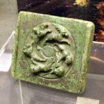 Belt-plate stamp of copper alloy found at Sheepen, Colchester, matching examples of such plates from Chichester (amongst others). Image: MCB Cast copper-alloy rectangular stamp with a green patina, depicting a hunt scene around a central boss.