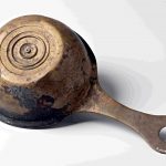 Underside view of a copper-alloy trulla or patera found in the Maas at Alphen (NLD) with an illegible stamp and a punctim ownership inscription >. C. ANCESTI C.VALERI CRIS LE(?)G XXII. Image: National Museum of Antiquities, Leiden (CC0 1.0) Underside view of a pan with moulded rings (perhaps to assist with heating) and a bronzey patina.