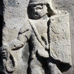Column base relief from Mainz depicting a legionary with a curved rectangular shield, helmet, and mail shirt with a split at the hem. His sword is worn on his left hip and in his right hand he holds a loop. Image: Carole Raddato (CC BY-SA 2.0) Legionary soldier moving from right to left holding a loop in his right hand and a shield (with wings and thunderbolt blazon and a tabula ansata) in his left.