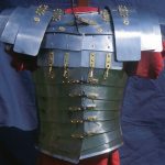 Complete Corbridge type B/C lorica segmentata viewed from the rear. Reconstructed by the Ermine Street Guard. Image: MCB Armour formed from steel strips with brass fittings displayed on a red tunic.