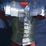 Complete Corbridge type B/C lorica segmentata viewed from the front. Reconstructed by the Ermine Street Guard. Image: MCB Armour formed from steel strips with brass fittings displayed on a red tunic.