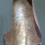 Interior view of a rear copper-alloy saddle horn from Newstead showing two inscriptions, one incised SIINIICIONIS (belonging to Senecio) and punctim XII (12). Image: MCB (CC BY_SA 2.0) Concave copper-alloy object with a rounded top, holes around its periphery, with a bronzey patina, and with scratched lettering and punched numerals.