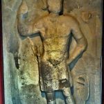 Relief of Mars from Housesteads depicted with his sword on his right hip and with the horizontal hand grip of his oval shield resembling those of the Dura shields. His helmet has a fore-and-aft crest and side plumes. Image: MCB Stone relief with a depiction of Mars leaning on his spear, held in his right hand, and with the rear face of his shield visible on the ground by his side.