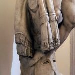 Detail of a side view of the Ludovisi Antoninus Pius statue showing a draped garment with lappets and pteryges, identified by Robinson as an arming doublet. Image: MumblerJamie (CC BY-SA 2.0) Depiction in marble of a garment draped over a tree stump with a Corinthian helmet at its base.