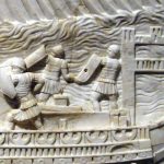 Detail of one of three joining relief panels from the Medinacelli reliefs depicting the battle of Actium showing eight biremes. It depicts two marines with curved rectangular shields and a third with a hexagonal shield. They also appear to wear pteryges over tunics, and body armour that resembles the strips usually employed to depict lorica segmentata. Image: Mark Landon (PD) Detail of a relief panel depicting a naval battle, identified as Actium, showing three marines on two ships.